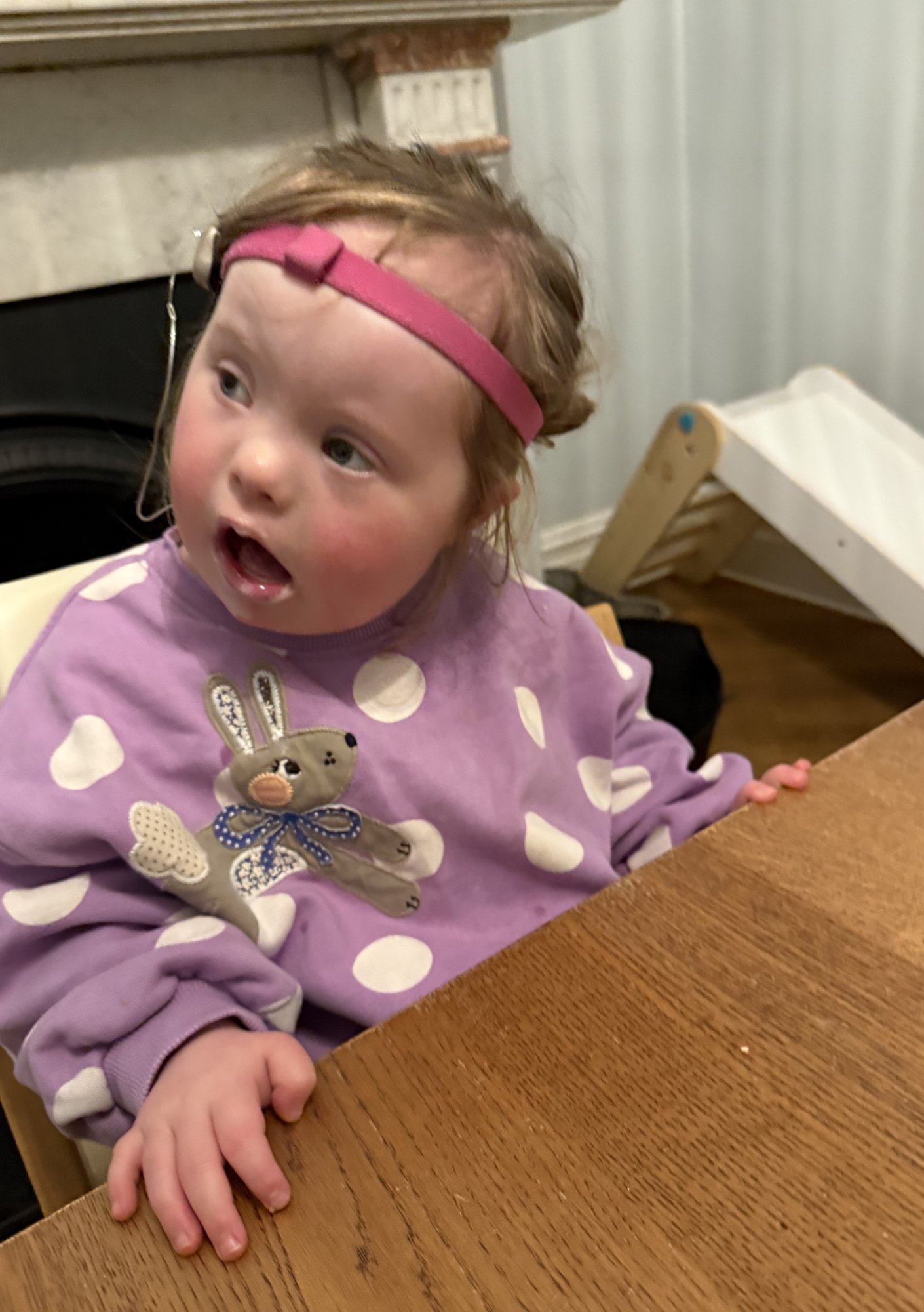 Child with Down syndrome sitting at table using hands for support, showing developing fine motor skills and stability in daily activities
