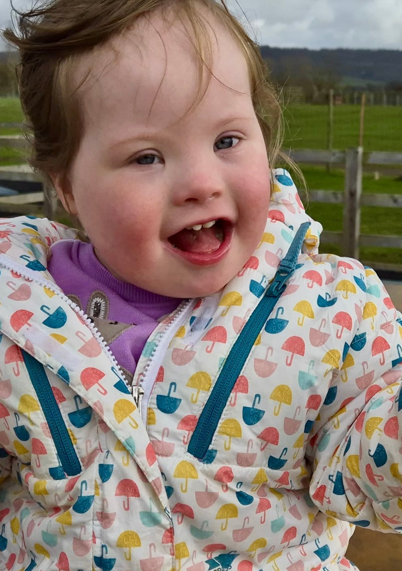 Toddler with Down syndrome smiling outdoors, showing confidence and participation in daily activities that support overall development