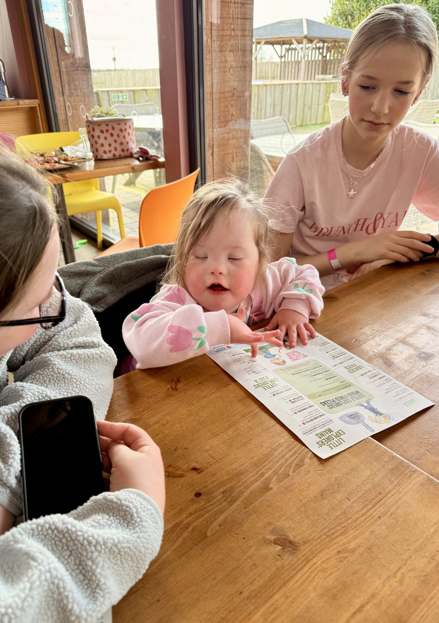 Child with Down syndrome reaching for paper on table, practising fine motor tasks, grasp and hand coordination with small objects