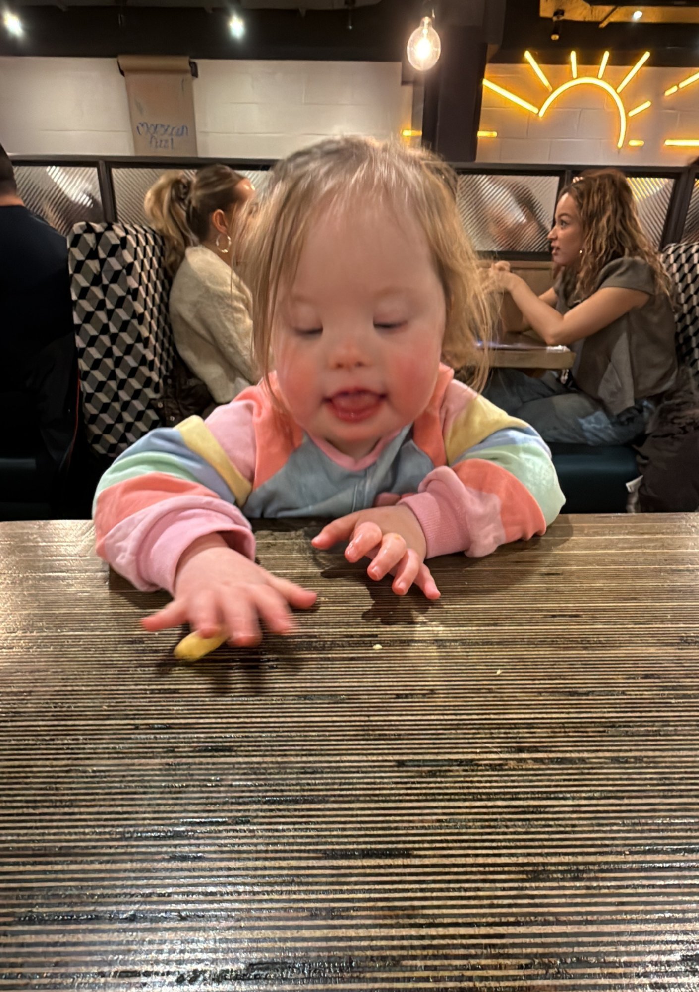 Toddler with Down syndrome reaching for small object on table to develop fine motor skills and hand coordination during feeding